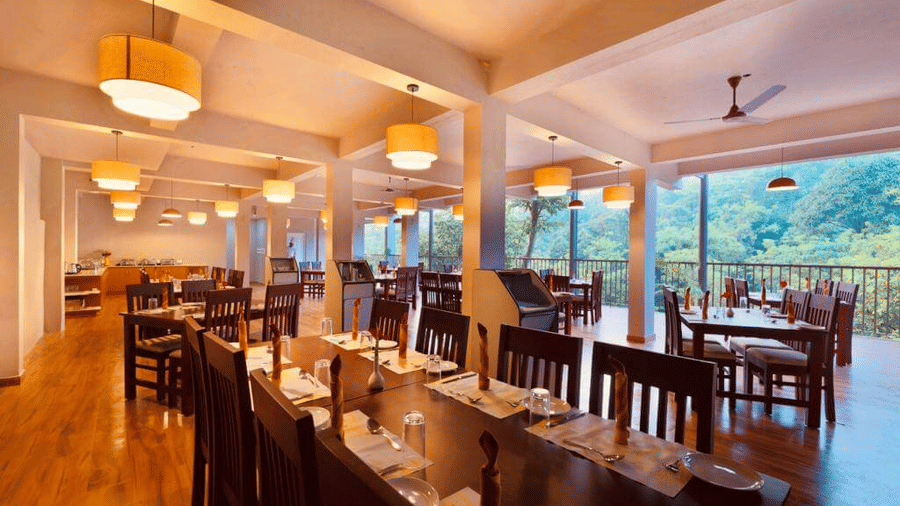 A restaurant with an open-air design and wooden furnishings.- Abad Brookside Lakkidi, Wayanad