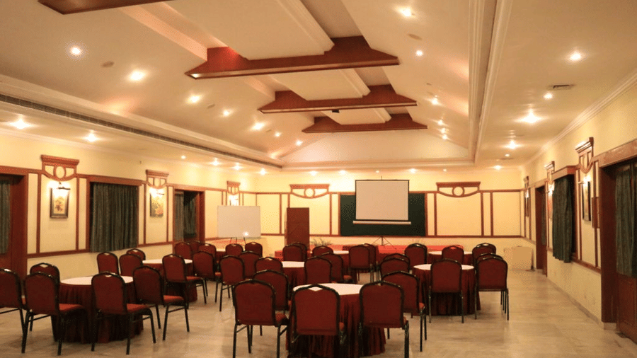 Indoor banquet hall with round tables and red chairs arranged for an event, featuring modern ceiling lights and decor - Black Thunder, Coimbatore