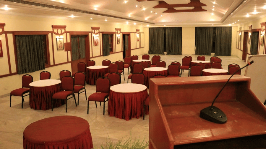 Modern indoor conference room with round tables and chairs arranged for meetings or events, complete with a podium and stage - Black Thunder, Coimbatore