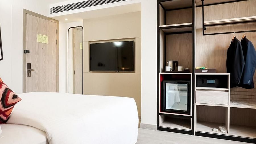 Hotel room interior featuring a wall-mounted TV, open wardrobe with hanging space, mini fridge, tea and coffee setup, safe, and a neatly made bed in the foreground - Golden Tulip, Lucknow