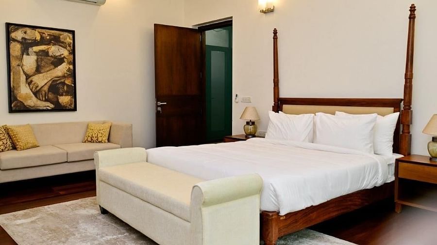 Shot of a king size bed in a fully furnished room with a cosy couch in the corner and wall mounted painting | Udman Luxe Villa