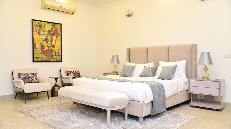 Image of a fully furnished pastel coloured room featuring a king size bed, a cosy corner with a sofa and a side table and lamp | Udman Luxe Villa