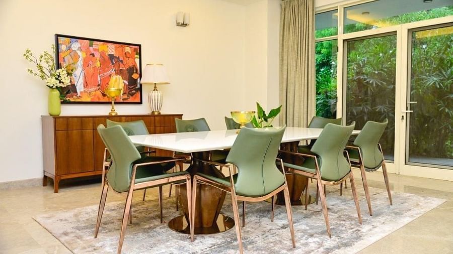 Shot of the dining room at the villa featuring a white table with green chairs around and wall mounted painting | Udman Luxe Villa