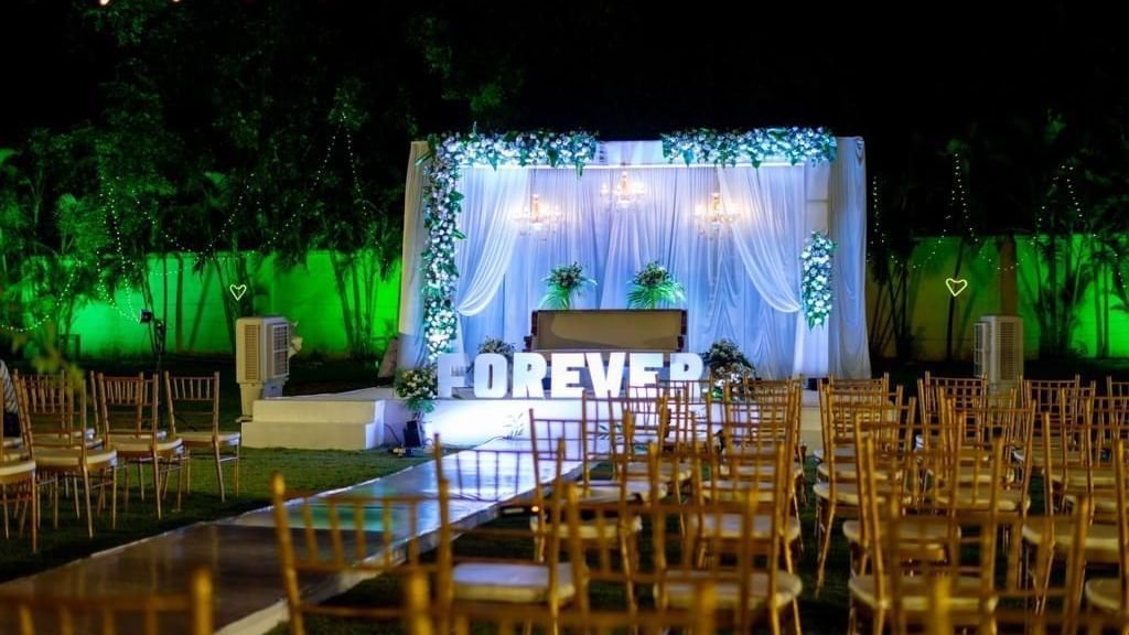 Evening view of outdoor seating facing a floral-lit stage with ‘FOREVER’ signage at Ilara Hotels & Spa, OMR, Chennai