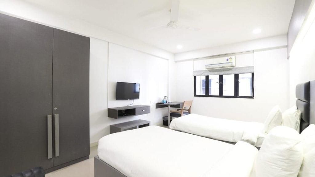 Corner view shot of the Premium Twin Room at Pravasa Ahmedabad featuring bright and minimalist interiors along with a wardrobe in the corner.