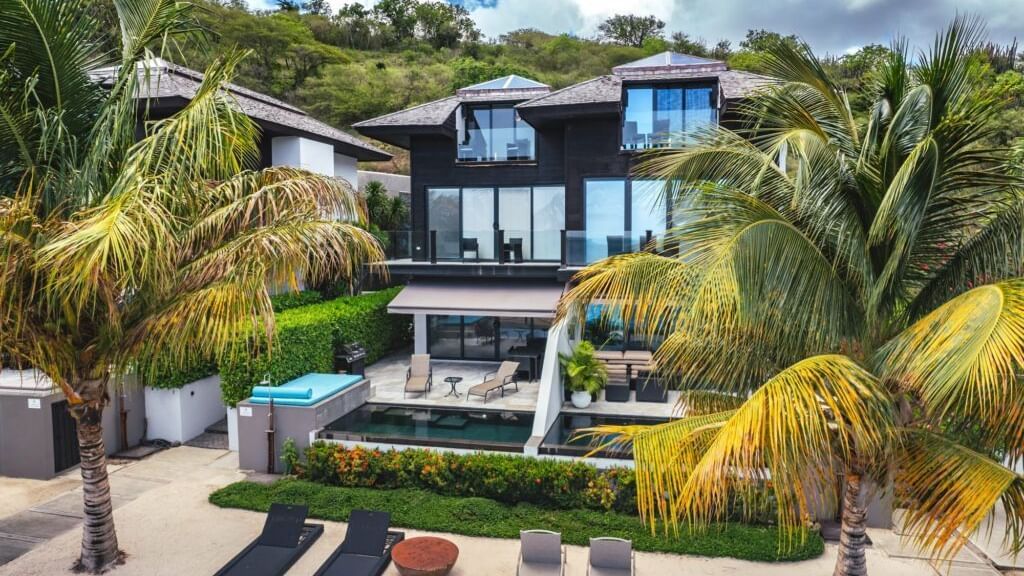 A wide angle shot of the villa with cars parked and trees all around.