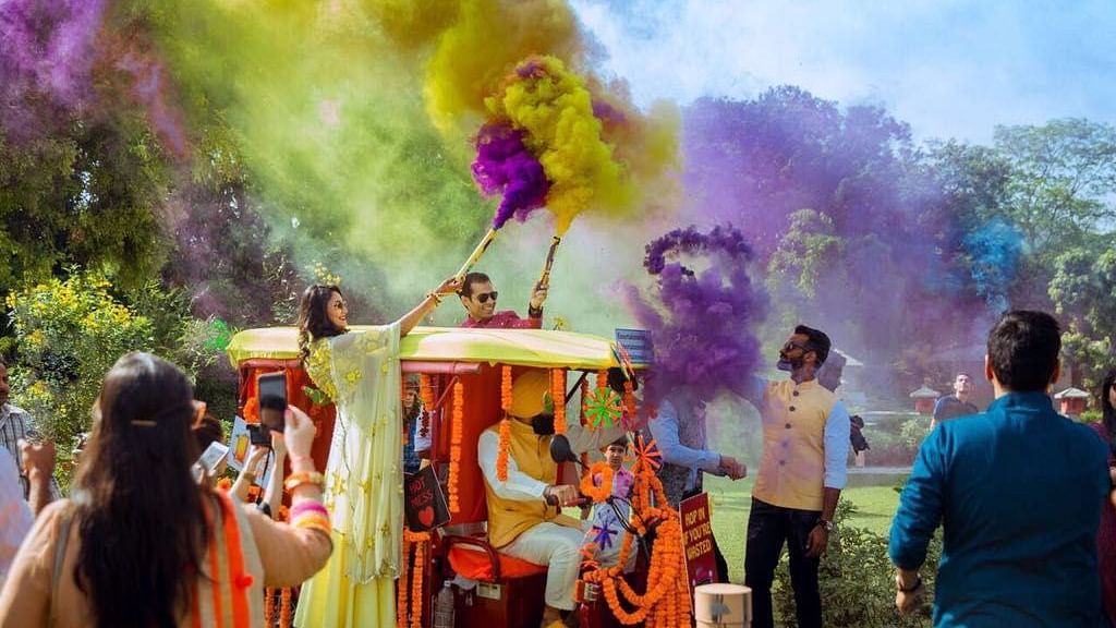 An image of people playing with colours in a lawn and two individuals standing on a carriage 