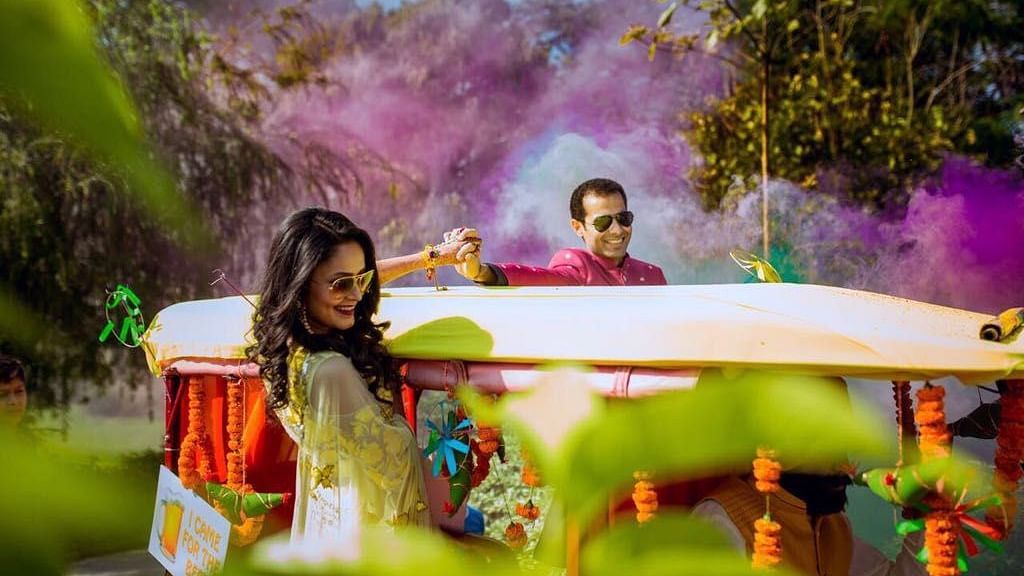An image of bride and groom on a carriage decorated with flowers and paper wheels