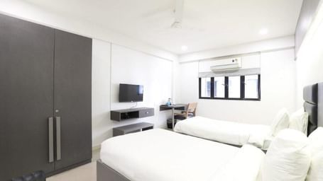 Corner view shot of the Premium Twin Room at Pravasa Ahmedabad featuring bright and minimalist interiors along with a wardrobe in the corner.