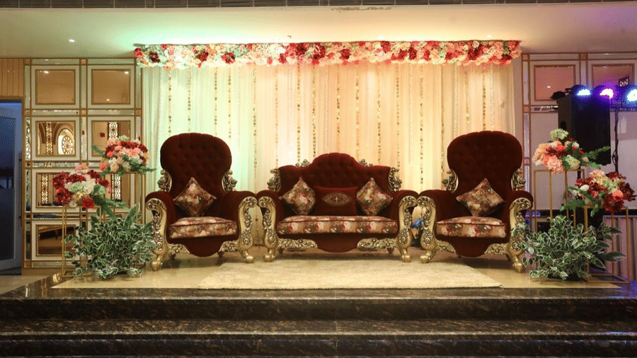 A wedding venue setup with two ornate looking chairs set up on a stage with other decorations on the side.