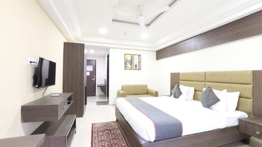 Full view shot of a brightly lit Premium Room at Pravasa Ahmedabad featuring a double bed and a wall mounted television placed opposite to it.