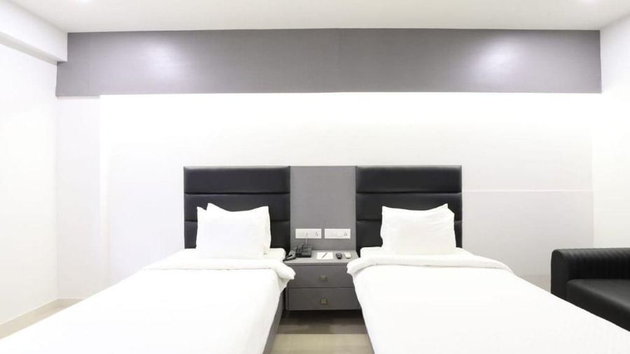 Front view of the twin bed cover with plain white sheets along with a bed side table in front of them in the Premium Twin Room at Pravasa Stay, Ahmedabad (Alba Premier).