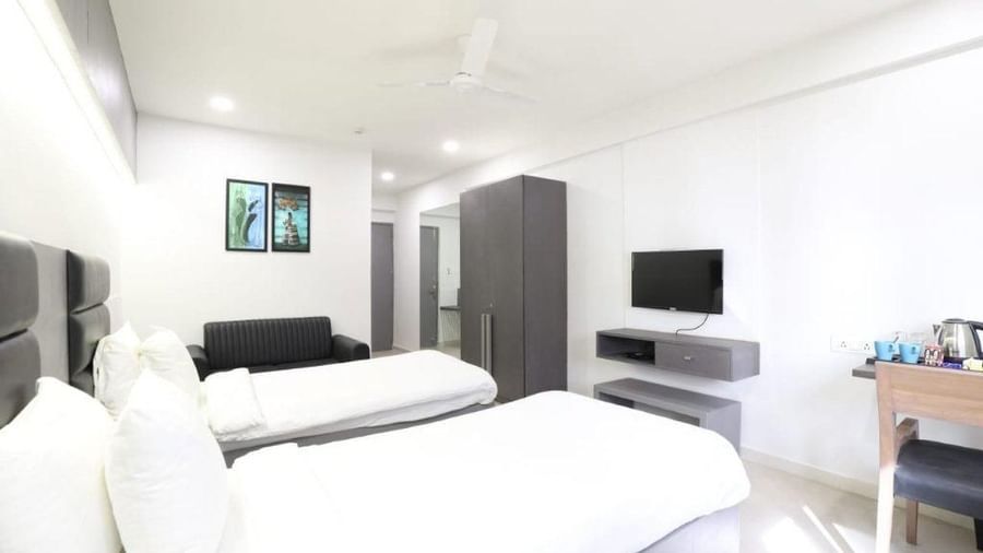 A wide-angle shot of the Premium Twin Room featuring 2 single beds along with a wardrobe and a wall-mounted television in front of it at Pravasa Stay, Ahmedabad (Alba Premier).