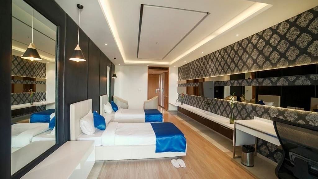  spacious hotel room at BNGV Grandeur Hotel and Banquets, with a long perspective showcasing the bed, a desk area, and modern architectural lines.