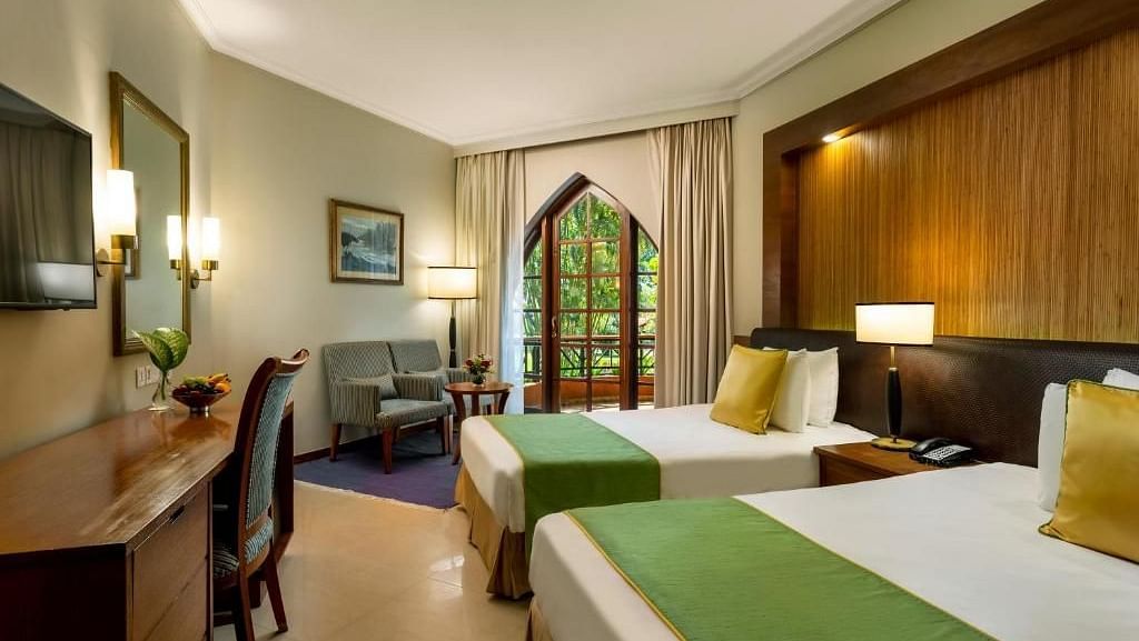 twin bed with golden pillow and green runner on it inside one of the rooms - Caravela Beach Resort Goa