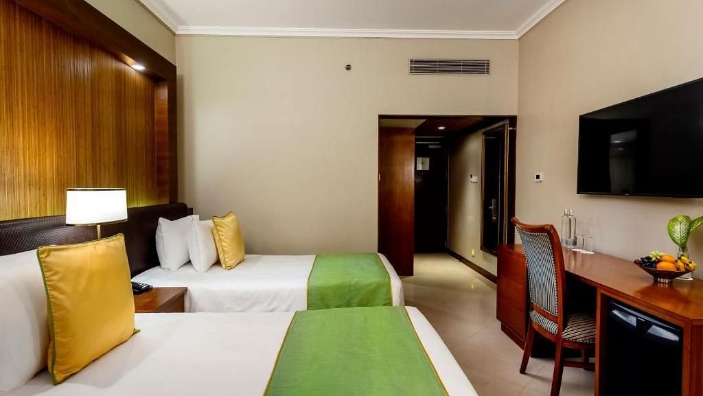 twin bed with golden pillow and green runner on it inside one of the rooms - Caravela Beach Resort Goa