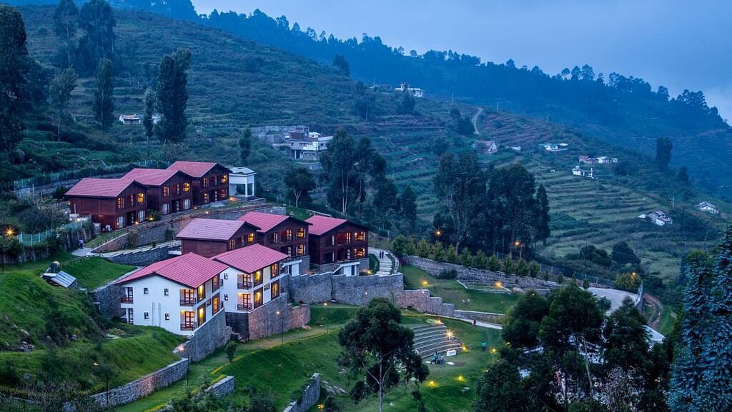 A drone shot of the GReaT Trails Kodaikanal By GRT Hotels property surrounded by lush greenery and trees with a clear sky