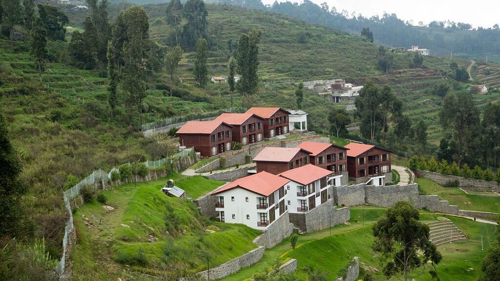 A drone shot of the GReaT Trails Kodaikanal By GRT Hotels property surrounded by lush greenery and trees with a clear sky