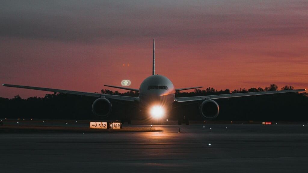 An airplane is seen on a runway at dusk with its landing lights illuminated.