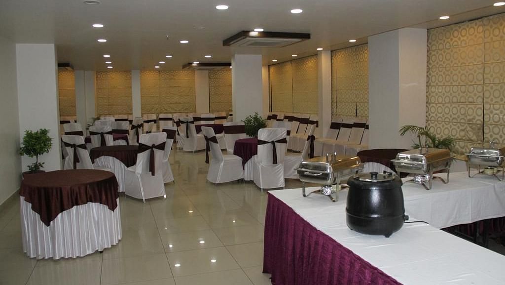 A banquet hall with round tables draped in white and brown and a buffet setup - TGI Apple Inn, Jaipur 