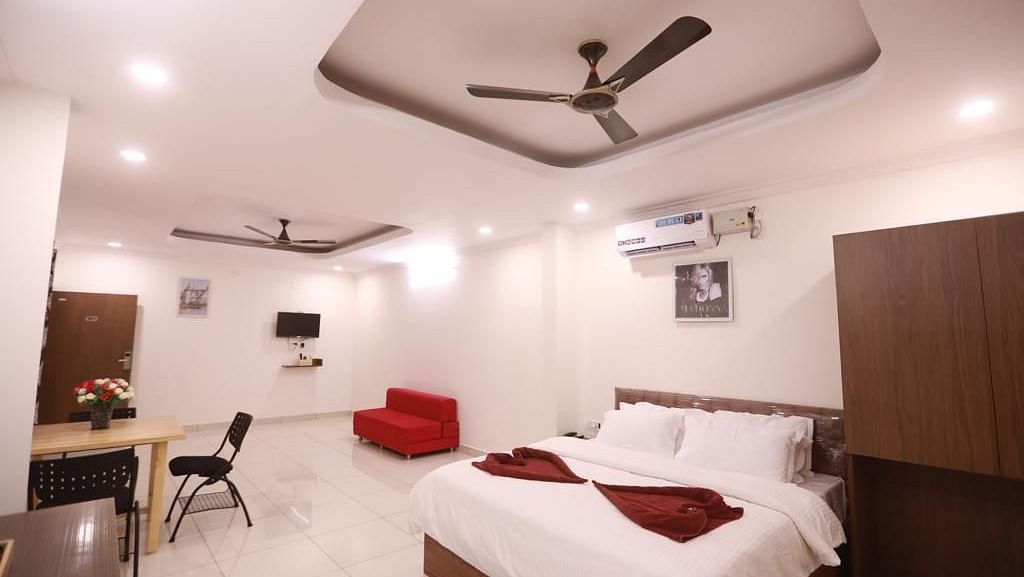 Large suite with a red sofa, a plush bed, a work desk, and  a chair | Vistar Resort, Bengaluru