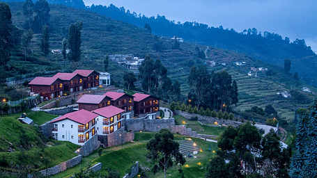 A drone shot of the GReaT Trails Kodaikanal By GRT Hotels property surrounded by lush greenery and trees with a clear sky