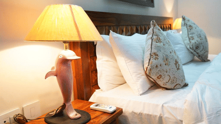 Bedside table of Lime Tree Hotels & Service Apartment Private Limited featuring a lamp and decorative pillows on a bed.