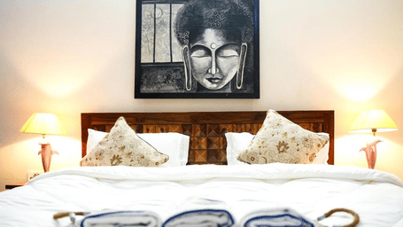 Bedroom of Lime Tree Hotels & Service Apartment Private Limited featuring a framed portrait artwork, white bedding, and bedside lamps.