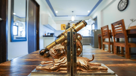 Lounge area of Lime Tree Hotels & Service Apartment Private Limited featuring a decorative telescope, a dining table, and wooden flooring.