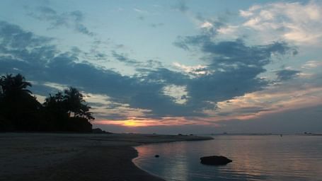 A serene beach side in the evening, featuring calm water and cloudy sky.