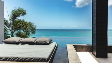 Modern lounge with a cushioned daybed overlooking a calm, turquoise ocean under a bright blue sky.