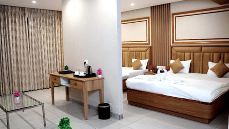 A Family Suite at the Prince ZENQ Xpress Resortt Rohtak featuring a main bedroom area with two large beds separated by a half-wall from a small living area with a console table and glass coffee tables.