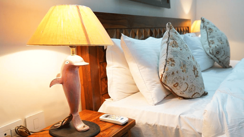 Bedside table of Lime Tree Hotels & Service Apartment Private Limited featuring a lamp and decorative pillows on a bed.