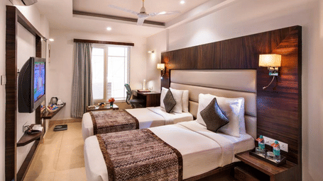 A stylish hotel room with twin beds, wooden floors, and large windows providing natural light at Lords Eco Inn Jayanagar Bangalore.