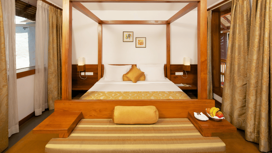 A hotel room featuring a wooden 4-poster bed and curtains with a bench at the foot of the bed | Le Pondy
