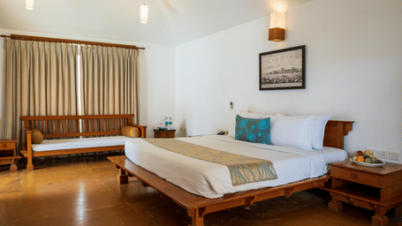 A hotel room featuring a large wooden bed, a framed picture on the wall, and a wooden bench near the window | Le Pondy