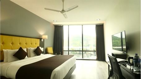 A bright hotel room with a yellow headboard, a large window overlooking a city view, and a flat-screen TV.IMG 6595
