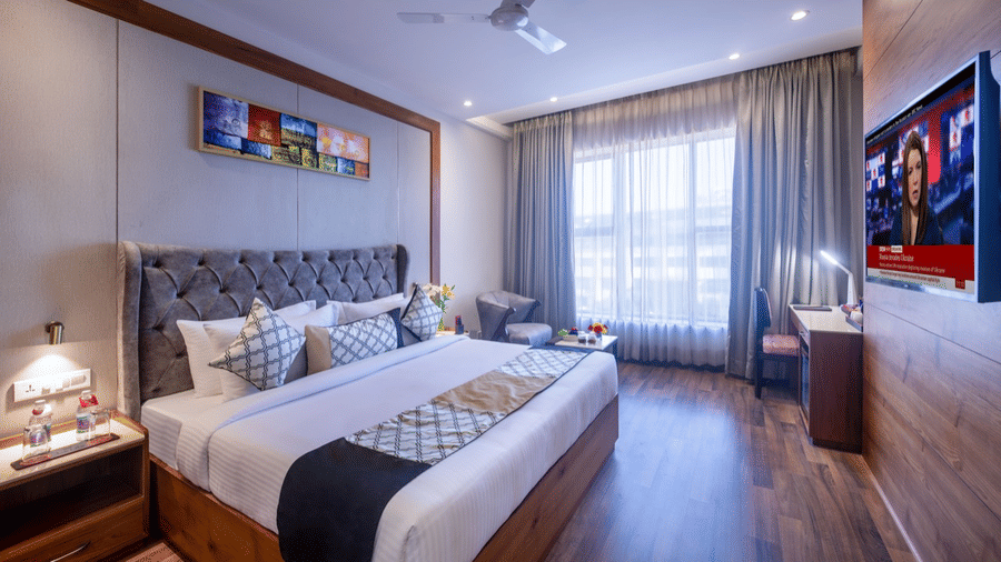 Executive room with a queen-sized bed, grey padded headboard, wall-mounted TV, large window, and minimalist decor.