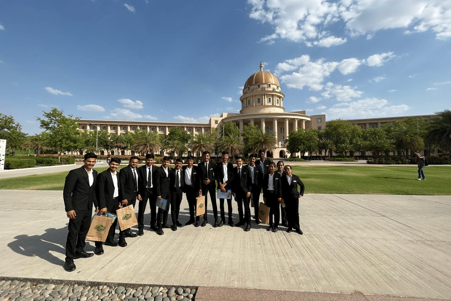 A group of people stands outside the college building. They pose together on a pathway next to a lawn.