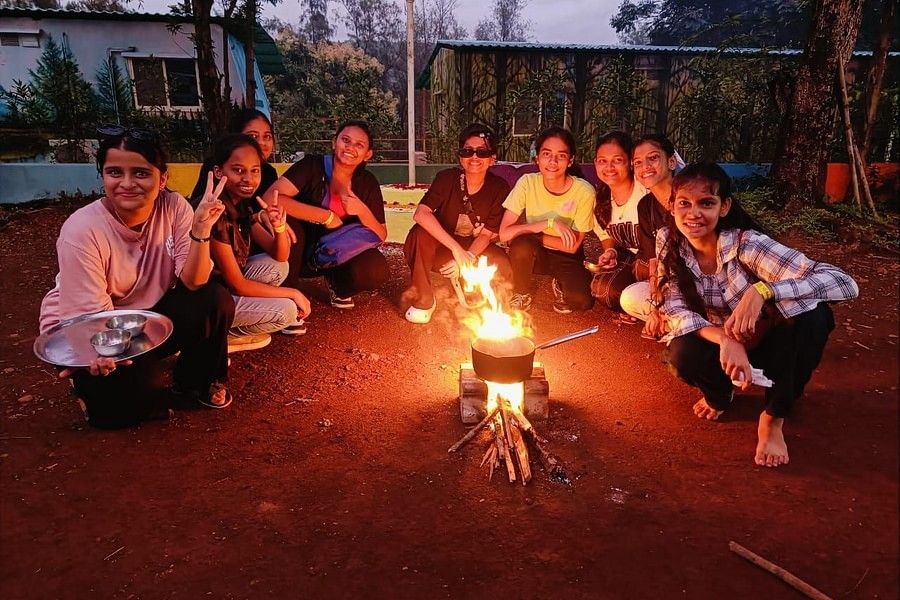 alt-text A group of teenage girls smiling while cooking using wooden stove on a late evening