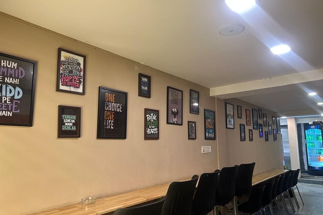 A hallway at The OnTime Hotel, Bangalore, with framed pictures on the wall and a long table with chairs.