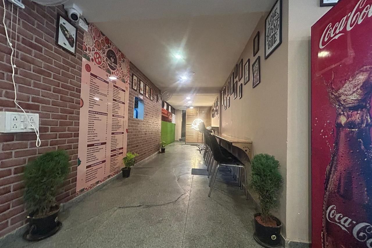 A view down a hallway at The OnTime Hotel, Bangalore, with exposed brick walls, a plant, and a red Coca-Cola vending machine.