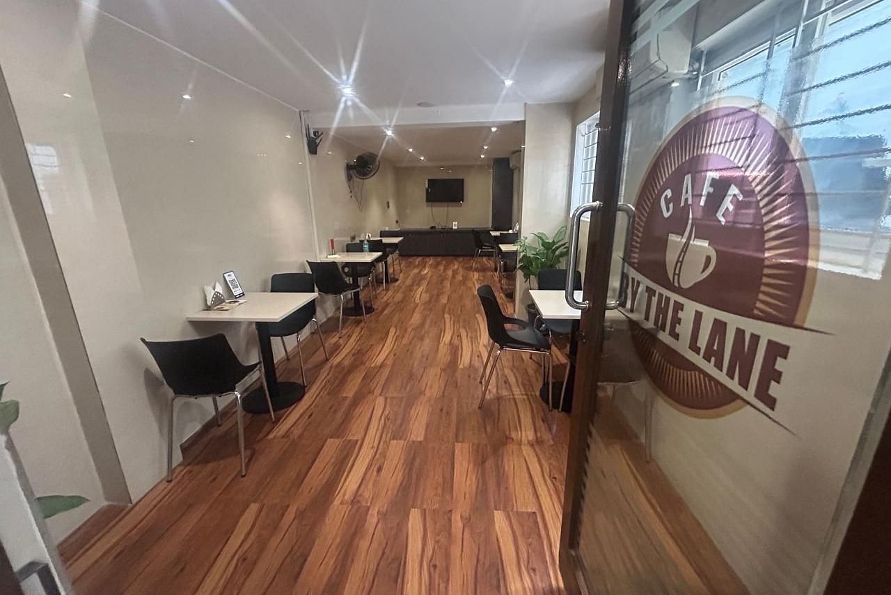A dining area at The OnTime Hotel, Bangalore, with tables and chairs, and a sign that says CAFE BY THE LANE..