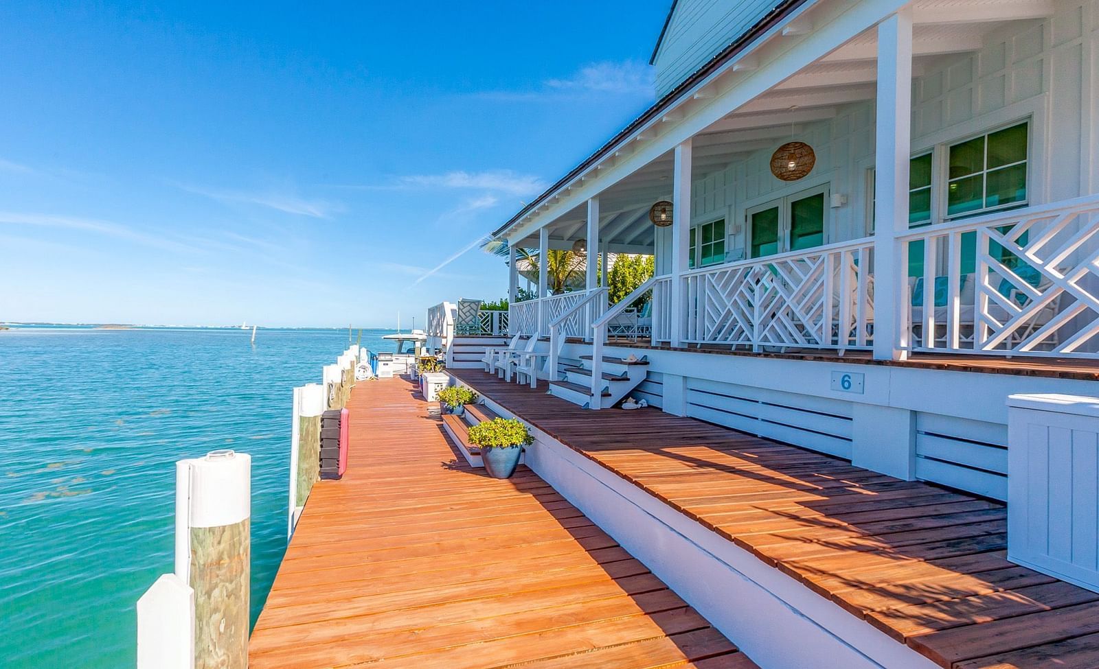 Waterfront wooden deck alongside a white coastal villa with seating, overlooking calm blue sea under a clear sunny sky at Abaco Inn
