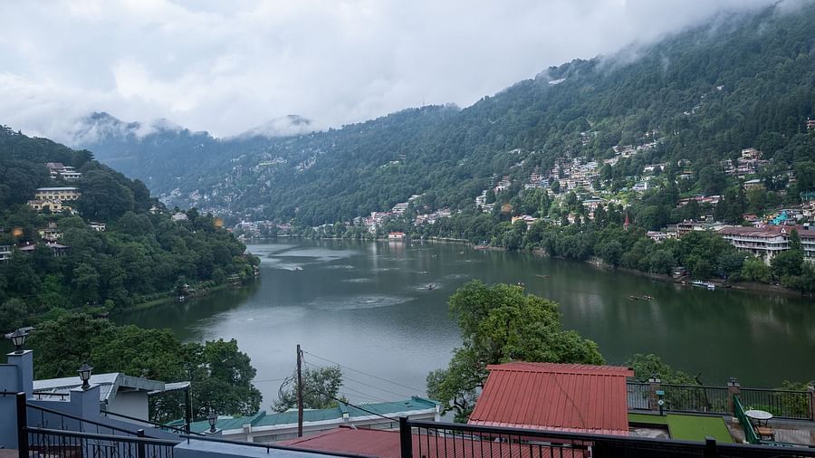 Atmospheric view from Himalaya Hotel, Nainital of mist-covered Naini Lake with traditional architecture, boats, and dramatic cloudy sky over mountain valley.