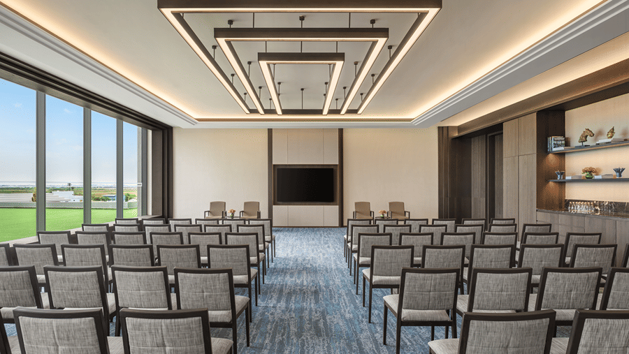 Council 3 meeting room in theatre-style seating with rows of grey chairs, a wall-mounted screen and square pendant lights at The Residency Signature Madurai.