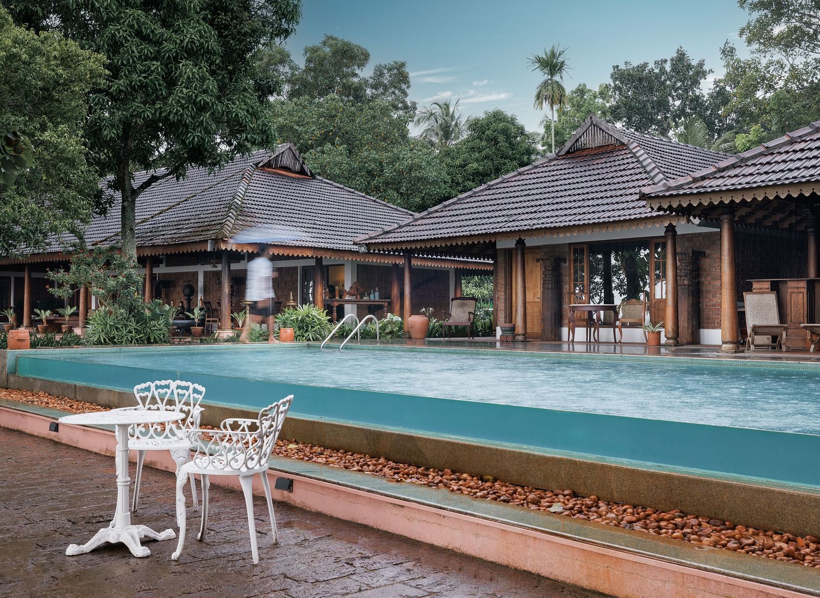A shot of the pool with chairs and table near it and the restaurant in the background - BluSalzz Villas - Muhamma Resort, Alleppey