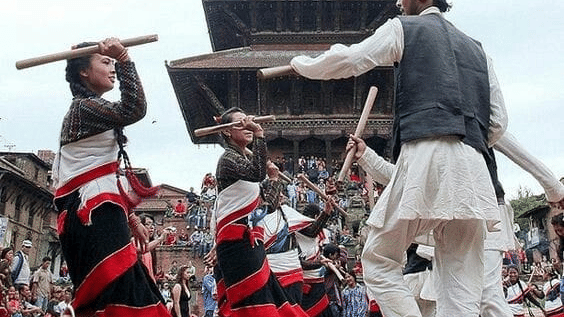 Local Newar youth in traditional white attire performing a stick dance during the Gai Jatra festival in a heritage square in Bhaktapur, Nepal.