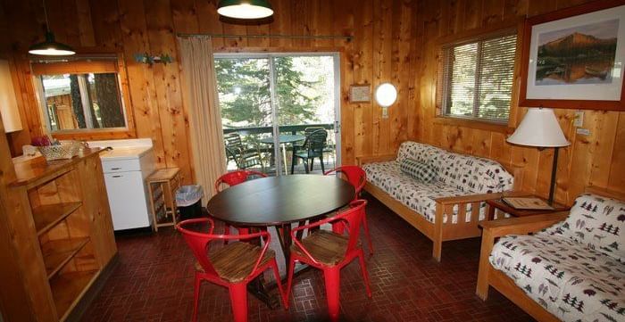 A rustic cabin interior with a dining table, chairs and two sofas. - Kit Carson Lodge & Restaurant