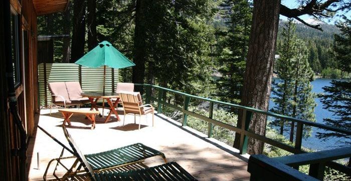 A spacious cabin deck with railings facing a serene lake. - Kit Carson Lodge
